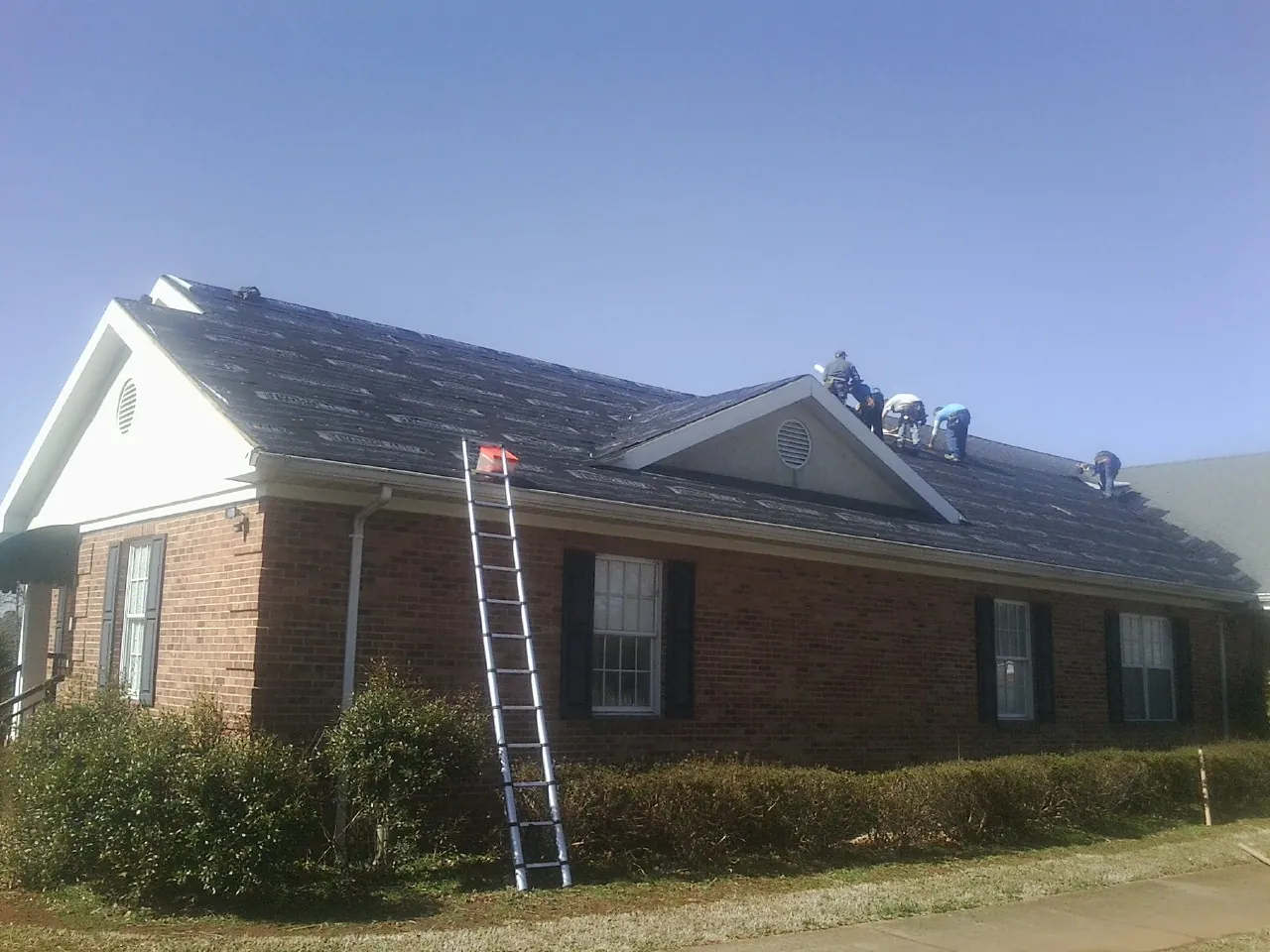 Crew tearing shingles off a brick ranch roof with a ladder set — Emergency Roof Repair work by our crew in Gordon