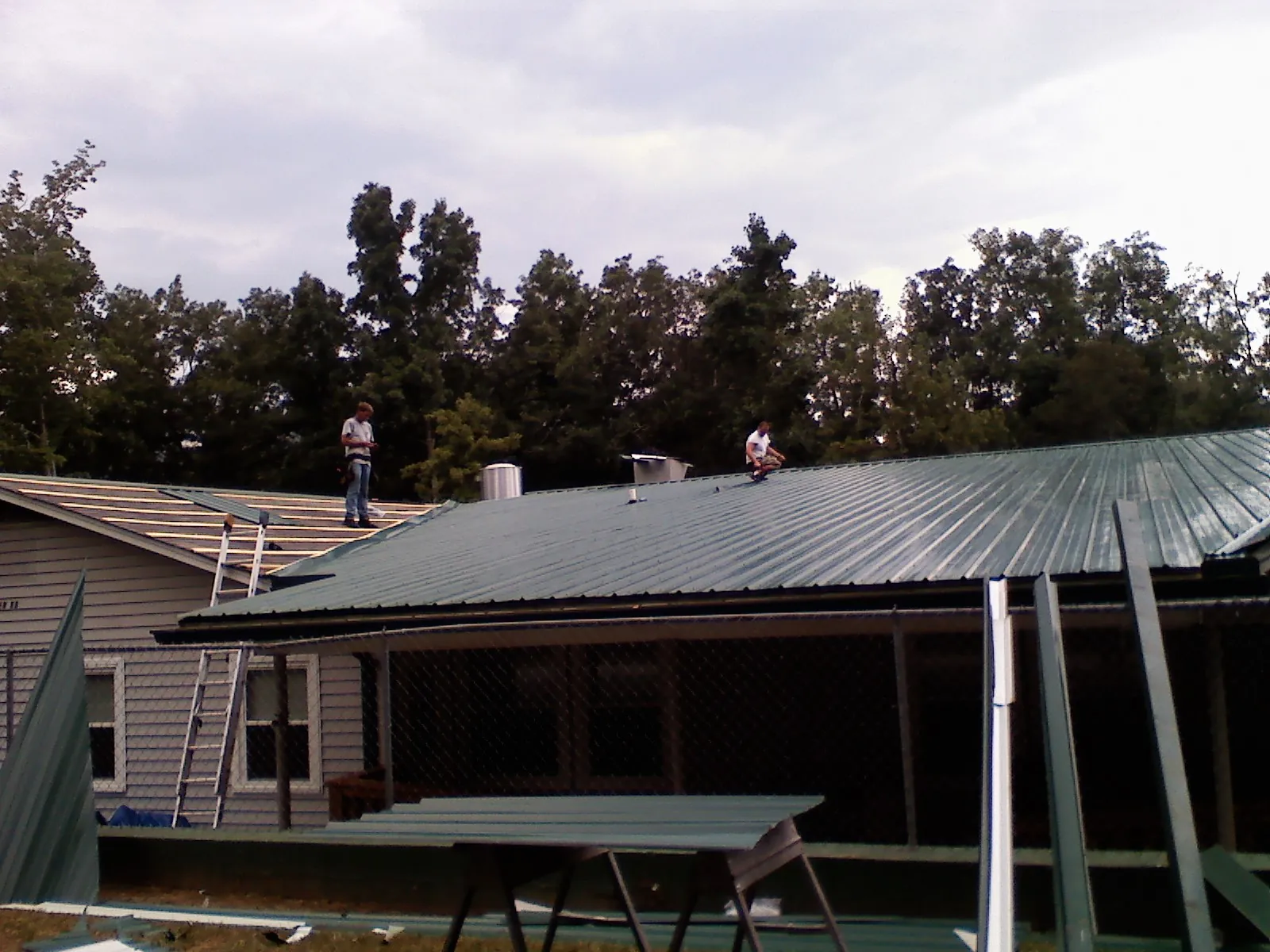 Two roofers installing green metal panels above a covered porch in Gordon