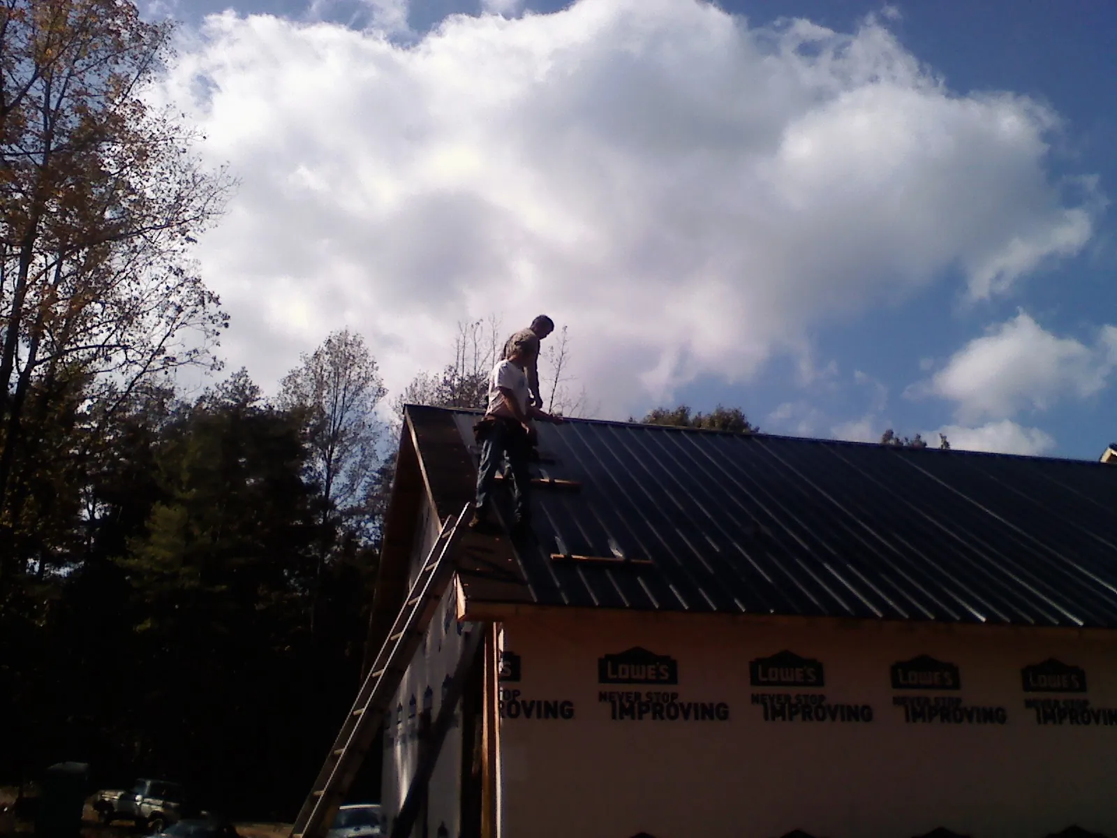 Roofer fastening dark metal panels high against a cloudy sky, from a Roof Inspection job in Gordon